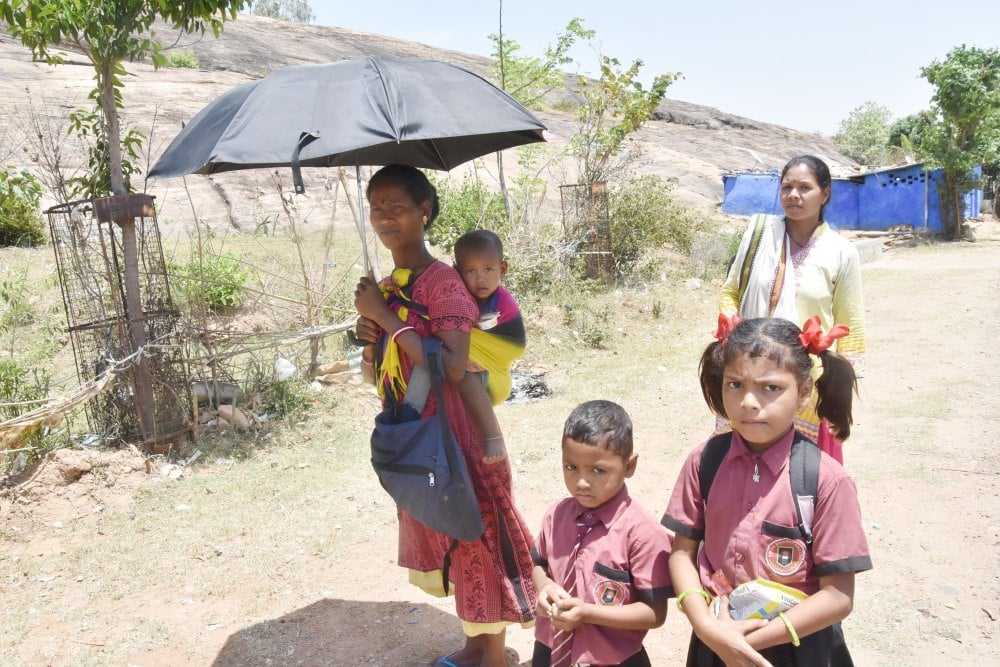 <p>A tribal woman carrying an umbrella and her child on her back along with her children returning from school amid a heatwave on a hot summer day, as the temperature crossed 43 degrees…